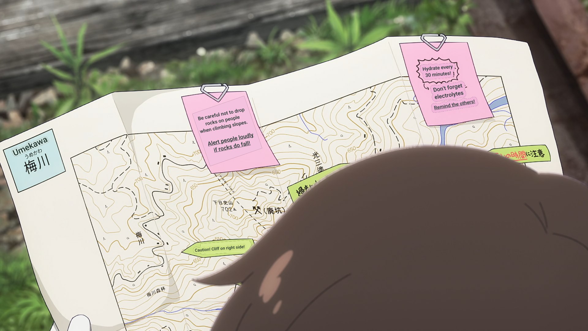 Close-up of a map being looked at with three post-it notes on it with advice about not making rocks fall when climbing and warning people when they do as well as to hydrate ever 30 minutes, not forgetting electrolytes and telling the others to do so too